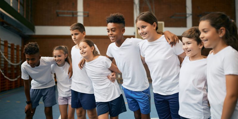 Group of happy school kids standing embraced as a team during physical education class at elementary school.