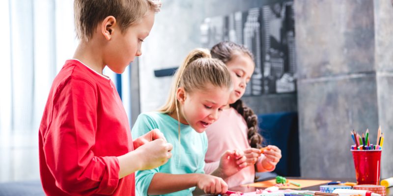Schoolchildren standing at table and playing with colorful plasticine